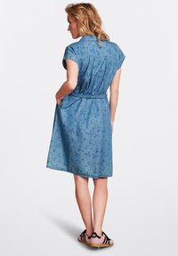 Jeansskjolklänning med korta ärmar, bälte i midjan och abstrakt blå mönster. Har sidofickor och knälång fåll.