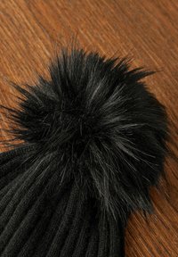 Must mustri müts, mille ülaosas on suur ja kohev must pom-pom. Peamine keha on tekstuuriga soonikdisainiga.