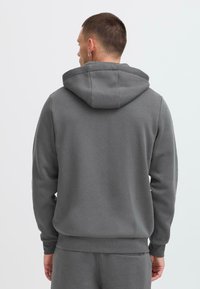 Sweat à capuche gris, avec une texture lisse, présentant des poignets et un ourlet côtelés. Design simple, avec un minimum de détails, vu de l'arrière.