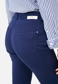 Zbliżenie na osobę w niebieskich dopasowanych spodniach z tylną kieszenią i w niebiesko-białą w paski koszulę włożoną do spodni.