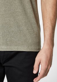 Kortärmad, olivgrön t-shirt i melerat tyg, uppvisad bredvid en hand, med rund halsringning och en avslappnad passform.