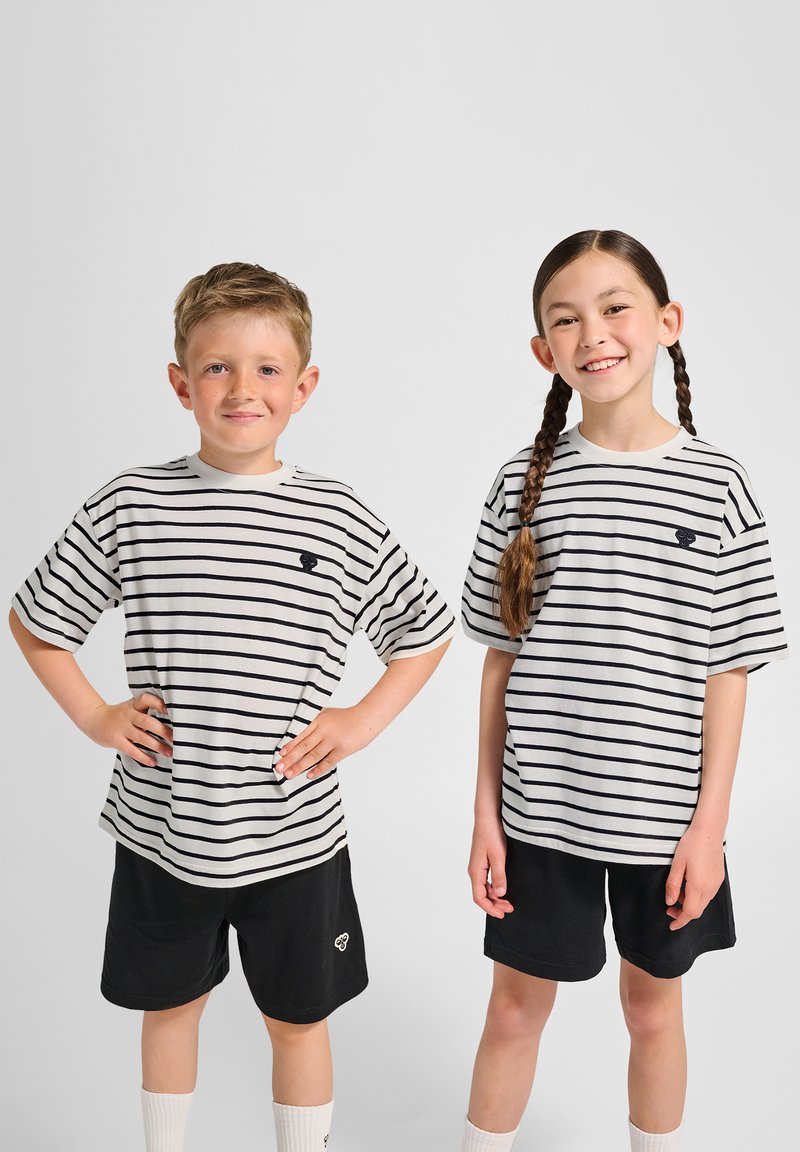 Randiga t-shirts i beige och marinblått, kombinerade med svarta shorts. Har korta ärmar och rund halsringning. Barnen har flätat och rufsigt hår.