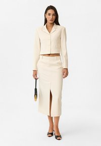 Afgekorte off-white blazer met een gelapte kraag en drie knopen, gecombineerd met een bijpassende rok tot de knie met een vooropening.