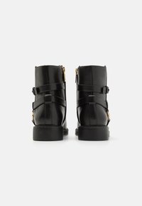 Bottines en cuir noir avec une finition lisse, dotées de accents de zip en or et de sangles réglables. Talon solide ; forme structurée.