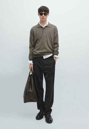 Maglione marrone lavorato a maglia con colletto, camicia bianca con bottoni sotto, pantaloni neri e una borsa in pelle scura. Indossato con scarpe nere e occhiali da sole.