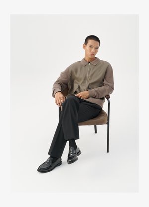 Herren Zip-Jacke in Erdtönen, mit einem strukturierten Stoff und übergroßen Taschen. Slim-Fit schwarze Hose und polierte schwarze Slipper.