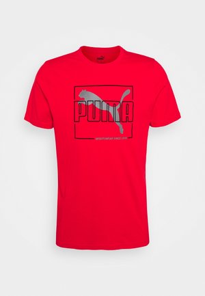 Červené bavlněné tričko s velkým černým a stříbrným logem "PUMA" a siluetou pumy, umístěnou uprostřed obdélníkového rámu.