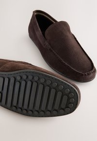 Mocassins en daim marron avec un dessus texturé, un bout arrondi et une semelle souple en caoutchouc noir dotée de stries horizontales.