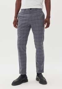 Pantalones de cuadros grises con un corte ajustado, que cuentan con bolsillos, una textura suave y un cierre de botón. Llevados con mocasines negros.