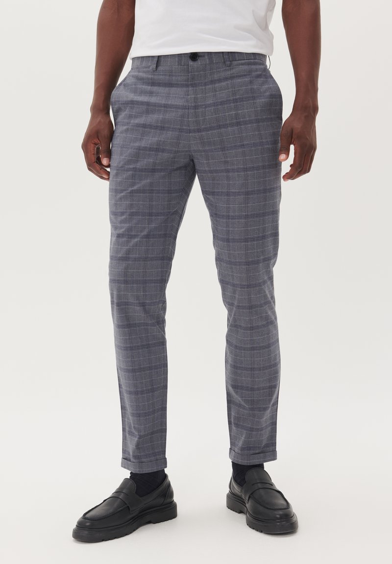 Pantalones de cuadros grises con un corte ajustado, que cuentan con bolsillos, una textura suave y un cierre de botón. Llevados con mocasines negros.