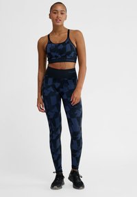 Blå mönstrad sport-bh och leggings-set i stretchigt material; har geometriska former och en bred midja; kombinerat med svarta träningsskor.