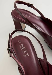 Vínové sandály na vysokém podpatku se slingback páskem. Hladká kožená úprava, čtvercový podpatek a branding "NEXT Forever Comfort" na stélce.