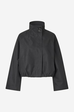 Lühendatud must jakk, millel on püstkrae, kaks eesmist nööpi ja elastne alumine äär; omaduseks raglaanvarrukad ja küljetaskud.