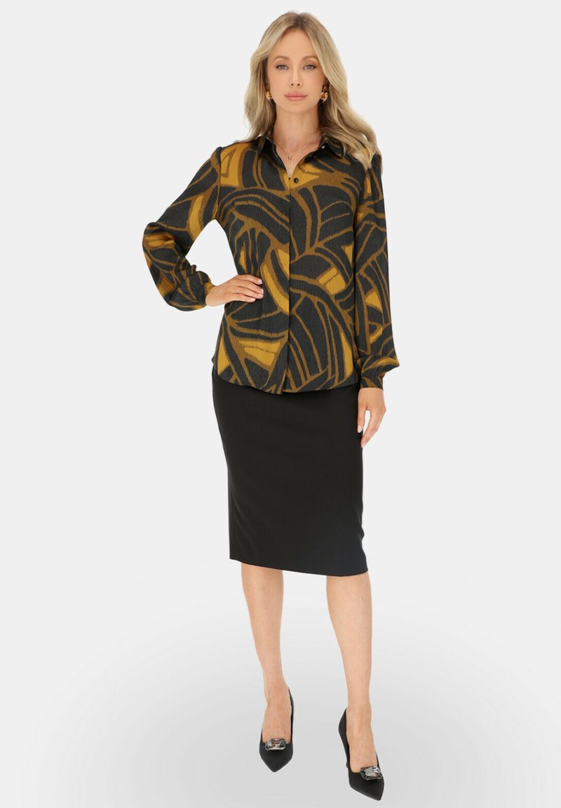 Czarna bluzka z długim rękawem i musztardowym wzorem abstrakcyjnym, w połączeniu z czarną spódnicą ołówkową i czarnymi szpilkami z dekoracyjnymi akcentami.