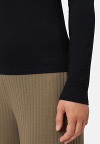 Černý dlouhý rukáv top z hladké tkaniny, s jemným logem na lemu. Kompletován se žebrovanými kalhotami olivové barvy.