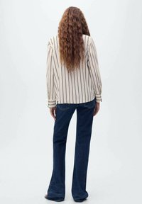 Crème gestreepte blouse met uitlopende mouwen, gecombineerd met donkerblauwe flared jeans. De outfit toont een losse pasvorm en een zachte stoftextuur.