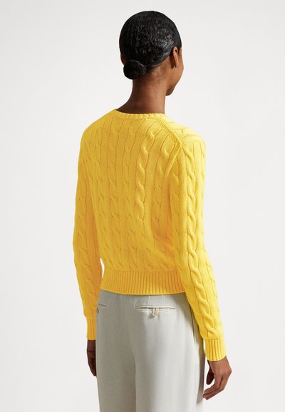 Rumeno pulover z vzorcem pletenja v kable s rebrastim robom in manšetami, z ohlapnim krojem. Pogled od zadaj prikazuje teksturirane podrobnosti in okrogel izrez na vratu.