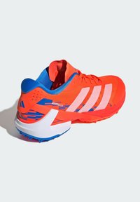 Red athletic shoe with blue accents, mesh upper, three white stripes, and a textured sole for grip. Features a streamlined design.
