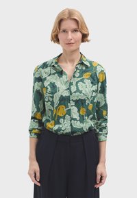 Camicia verde a fantasia con dettagli gialli, caratterizzata da un colletto, maniche lunghe arrotolate ai polsini e chiusura con bottoni.