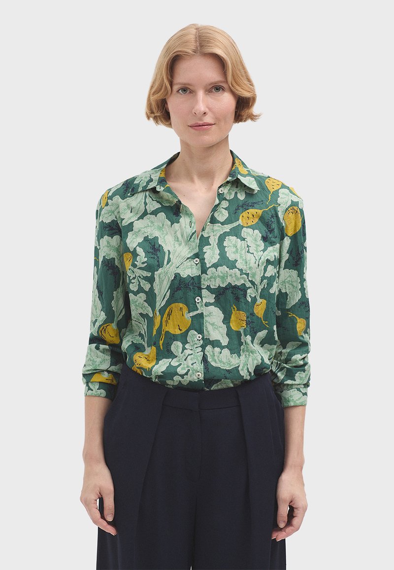 Camicia verde a fantasia con dettagli gialli, caratterizzata da un colletto, maniche lunghe arrotolate ai polsini e chiusura con bottoni.