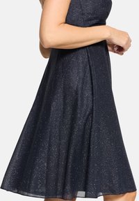 Robe bleu marine foncé à silhouette évasée, en tissu texturé avec des paillettes subtiles, dotée d'un corsage ajusté et d'un ourlet à hauteur des genoux.