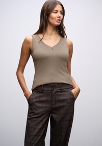 Top senza maniche color marrone chiaro con scollatura a V e due bottoni, abbinato a pantaloni marroni a fantasia con sottili strisce e una vestibilità comoda.