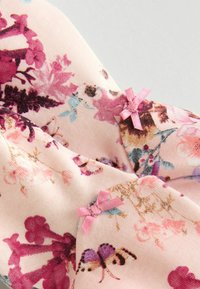Tessuto floreale in un delicato rosa, con dettagli di fiori e farfalle, impreziosito da due piccoli fiocchi rosa su ciascun lato.