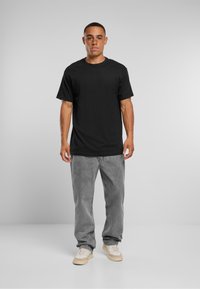 Maglietta di cotone nera con scollo rotondo, abbinata a jeans denim grigi larghi e sneakers beige. Design semplice e casual senza motivi.