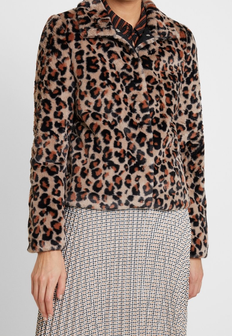 Veste en fausse fourrure à imprimé léopard portée sur une chemise rayée et une jupe pied-de-poule, montrant la taille et les bras.