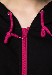 Felpa nera con zip, caratterizzata da una cerniera fucsia e lacci abbinati, dotata di occhielli in metallo e una piacevole texture di tessuto morbido.