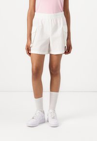 Hvite shorts med elastisk midje og sidelommer, laget av bomull, med en avslappet passform, kombinert med hvite joggesko og lysegrå sokker.