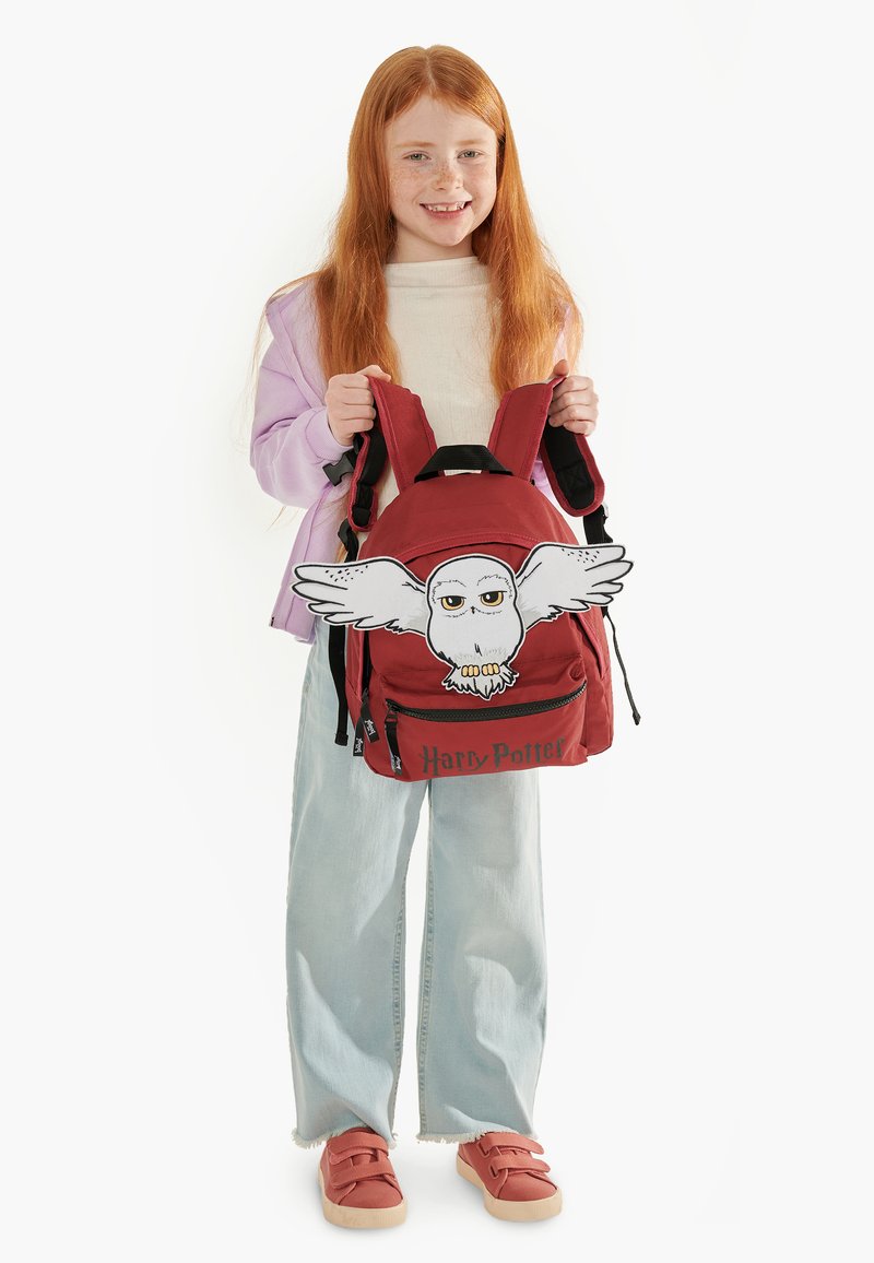 Zaino rosso con un design di un gufo bianco con le ali spiegate. "Harry Potter" è stampato in nero sul davanti.