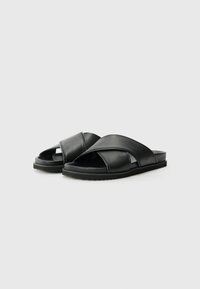 Sorte svarte lærsandaler med kryssremdesign, flat såle og teksturert grep for stabilitet. Glatt overflate med minimalistiske detaljer.