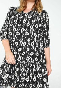 Robe noire à motif floral blanc, manches courtes bouffantes, encolure en V, jupe à volants, tissu léger, avec un ourlet évasé.