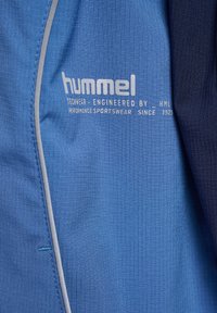 Blå och mörkblå sporttopp med en texturerad yta, med grå detaljer och logotyp. Materialet verkar lätt och funktionellt.