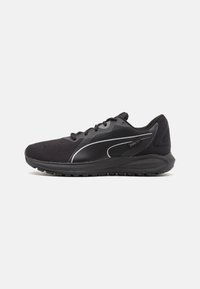 Zapatilla deportiva negra con parte superior de malla, diseño texturizado, acentos reflectantes y una suela de goma gruesa. Presenta cordones y un cuello acolchado.