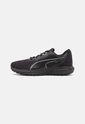 Zapatilla deportiva negra con parte superior de malla, diseño texturizado, acentos reflectantes y una suela de goma gruesa. Presenta cordones y un cuello acolchado.