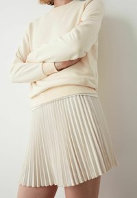 Crème sweatshirt van gladde stof, gecombineerd met een lichtbeige geplooide rok. Beide hebben een zachte textuur en een minimalistisch ontwerp.