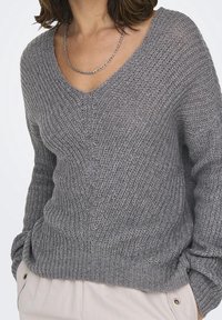 Grauer Strickpullover mit V-Ausschnitt, strukturiertem Muster und langen Ärmeln. Der Stoff wirkt weich und leicht locker sitzend.