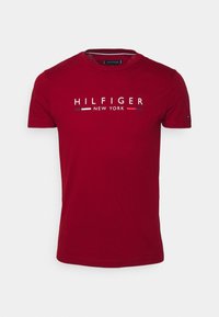 Rotes Baumwoll-T-Shirt mit dem „HILFIGER NEW YORK“-Logo in Weiß, akzentuiert mit blauen und roten Streifen. Mit kurzen Ärmeln und Rundhalsausschnitt.