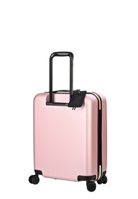 Harde roze koffer met een zwart uitschuifbaar handvat en vier wielen. Voorzien van een zwart bagagelabel en gouden ritssluitingen.