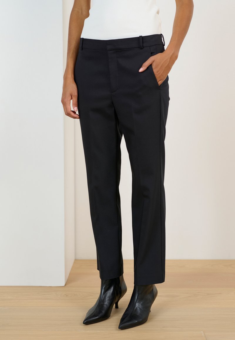 Czarne spodnie damskie o gładkim wykończeniu tkaniny, prostym kroju nogawek i bocznych kieszeniach, zestawione z czarnymi, szpiczastymi botkami za kostkę.