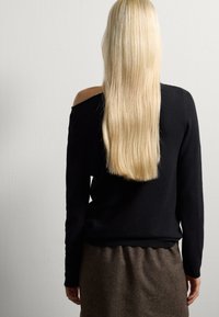 Maglione nero off-shoulder con maniche lunghe, realizzato in tessuto knit, abbinato a una gonna marrone strutturata. Capelli lunghi e lisci.