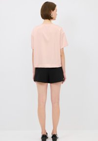 Top rosa a maniche corte con un design rettangolare, realizzato in tessuto morbido. Abbinato a pantaloni corti neri, creando un contrasto di colore e texture.