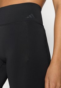 Czarne legginsy wykonane z elastycznego materiału, z wysokim paskiem, widocznymi szwami oraz małym logo w górnym rogu.