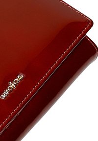 Portefeuille en cuir rouge foncé brillant avec des coutures visibles et un petit logo de marque argenté dans un coin.