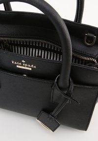 Borsa Kate Spade in pelle nera con zip dorata, fodera interna a righe, maniglie doppie e etichetta in pelle attaccata.