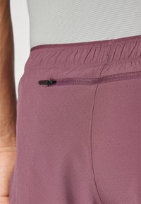 Shorts de sport violet clair avec une poche zippée, une taille élastique et une texture perforée pour la respirabilité.