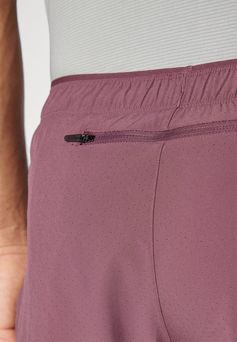 Pantalones cortos deportivos morados con una superficie texturizada, cuentan con un bolsillo con cremallera y una cinturilla elástica para mayor comodidad. Diseño perforado para transpirabilidad.