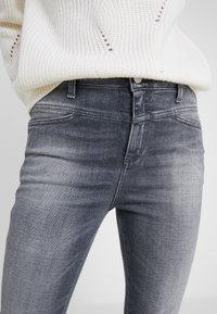 Jeans de denim ajustados y elásticos en un color gris desgastado, con un diseño clásico de cinco bolsillos y un ligero desgaste en los muslos.